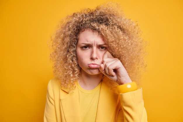 Free photo sulking crying woman has depressed bad mood wipes tears complains about difficult life whins with upset expression wears stylish clothes isolated over yellow wall. negative emotions concept