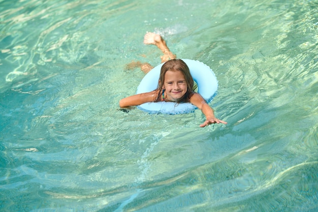 Summer activity. Sweet little girl swimming on a tube and smiling