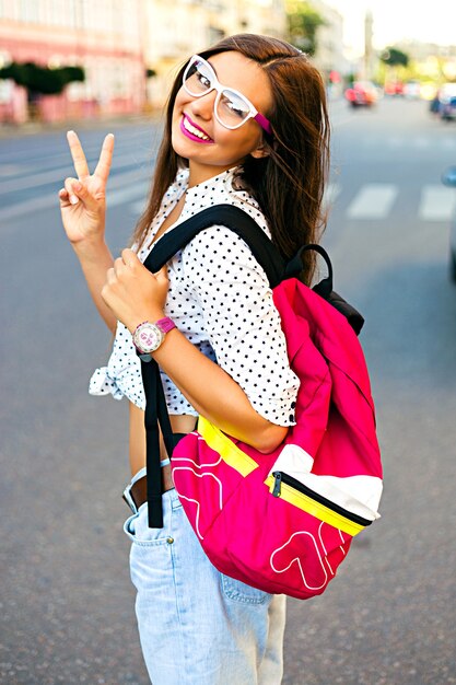 Summer city portrait of stylish teen girt, traveling alone with backpack, having nice day in new town, enjoy her vacation, wearing backpack, hipster glasses and casual look, joy, emotions