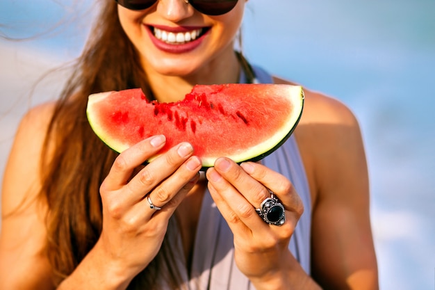 Summer close up details of woman with pretty smile holding a piece of sweet tasty watermelon, vegan food, perfect meal on the beach.