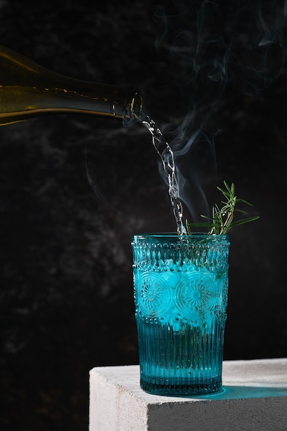 Summer cocktail with ice, lime and rosemary with smoke on white concrete stand