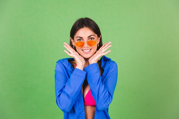 Summer fit sporty woman in pink bikini, blue shirt and orange sunglasses on green, happy cheerful joyful positive