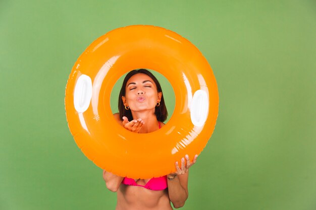 Summer fit sporty woman in pink bikini and bright orange inflatable ring round on green, happy cheerful excited joyful positive