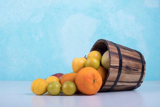 Летние фрукты смешивают из деревянного ведра на синем.