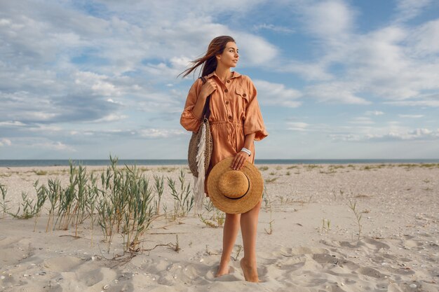 ストローバッグを保持しているジャンプと浮気のトレンディなリネンドレスの美しいブルネットの女性の夏のイメージ。海の近くの週末を楽しんでいるかなりスリムな女の子。