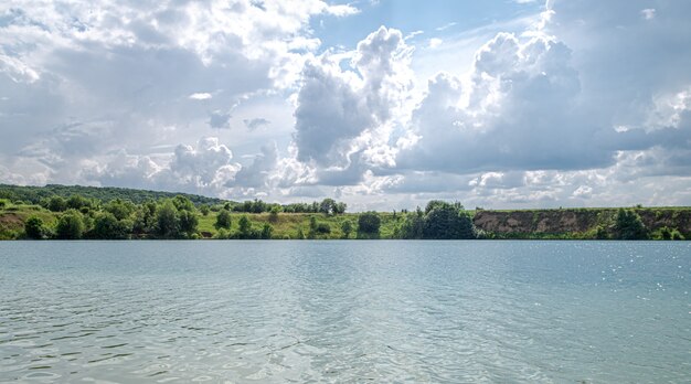 Летний пейзаж в сельской местности с рекой, лесом и облаками.