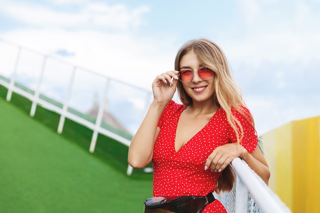 Summer lifestyle portrait of beautiful blonde woman posing in park.