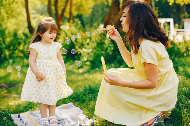 in a summer park near green trees, mom walks in a yellow dress and her little pretty girl