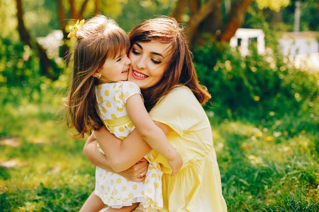 in a summer park near green trees, mom walks in a yellow dress and her little pretty girl