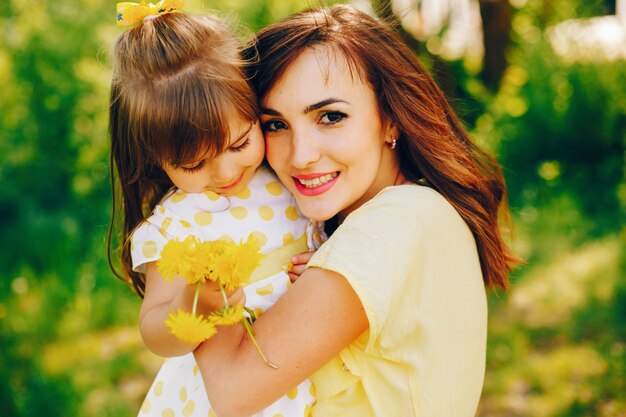 in a summer park near green trees, mom walks in a yellow dress and her little pretty girl