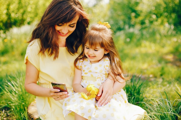緑の木の近くの夏の公園では、お母さんは黄色のドレスと彼女の小さなかわいい女の子の中を歩いています