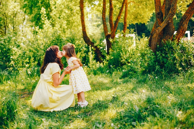 in a summer park near green trees, mom walks in a yellow dress and her little pretty girl