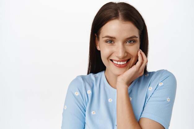 Summer people. Close up of beautiful adult woman in cute and tender blue blouse, smiling white teeth, blushing and giggle romantic, touching face, white background.