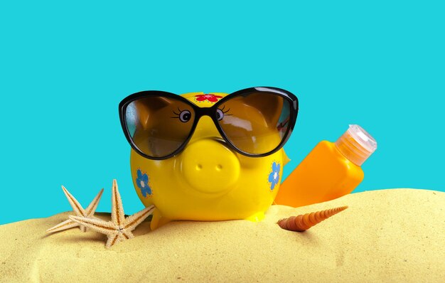 Summer piggy bank with sunglasses on the beach