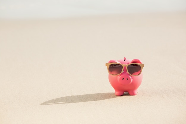 Summer piggy bank with sunglasses on sand