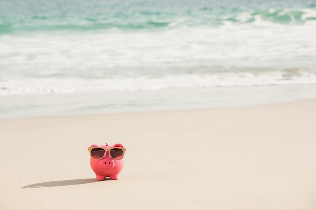 Free photo summer piggy bank with sunglasses on sand