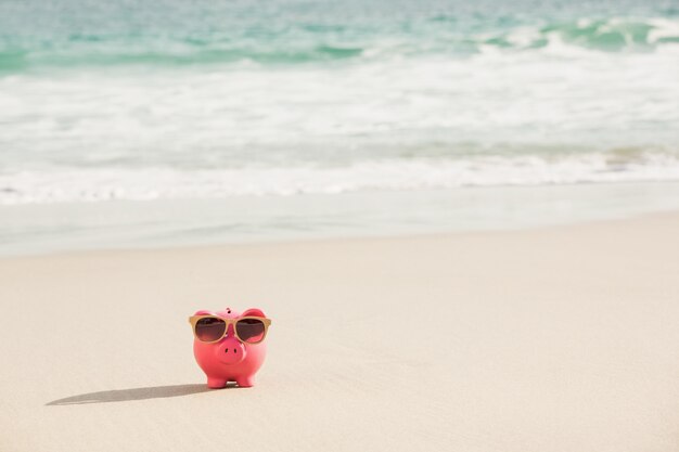 Summer piggy bank with sunglasses on sand