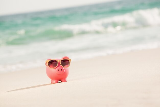 Summer piggy bank with sunglasses on sand