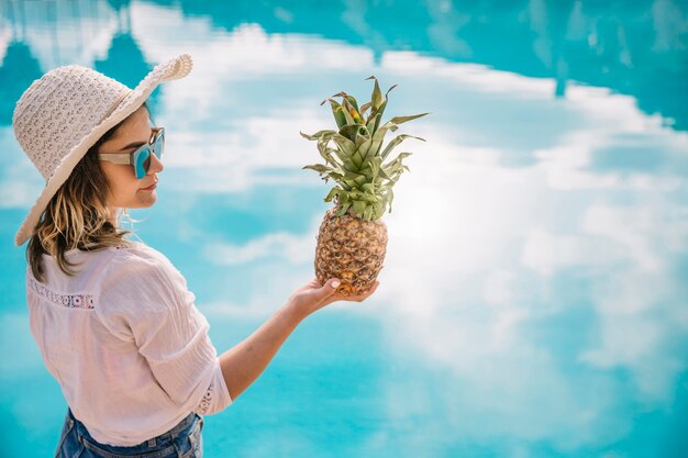 Концепция лета и бассейна с женщиной, держащей ананас