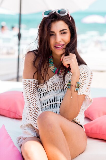 Summer portrait of beautiful brunette woman chilling in the beach club Tropical acsessories