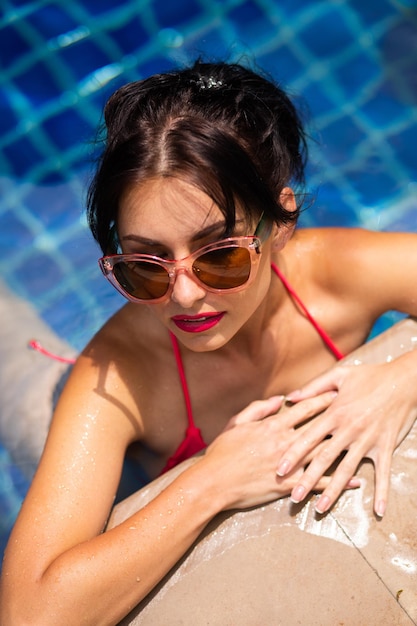 スイミングプールで楽しんでいるビキニのブルネットの女性の夏の肯定的なportrsit