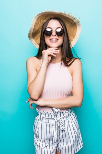 Summer travel woman in hat and sunglasses ready for feast trip and party isolated on blue wall.. Attractive smiling girl thinking of holiday. Summer mood.