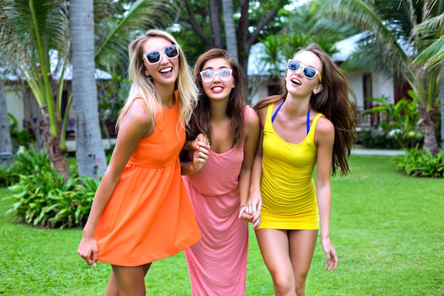 Летний тропический образ жизни портрет трех счастливых девушек-лучших друзей, весело проводящих время на открытом воздухе, в ярких сексуальных платьях, пляжном стиле отпускной вечеринки, экзотическом саду, модных солнцезащитных очках, расслаблении, радости