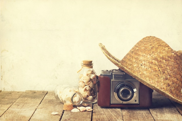 夏または休暇のコンセプト。古いヴィンテージカメラと木製の背景にシェルと麦わら帽子。