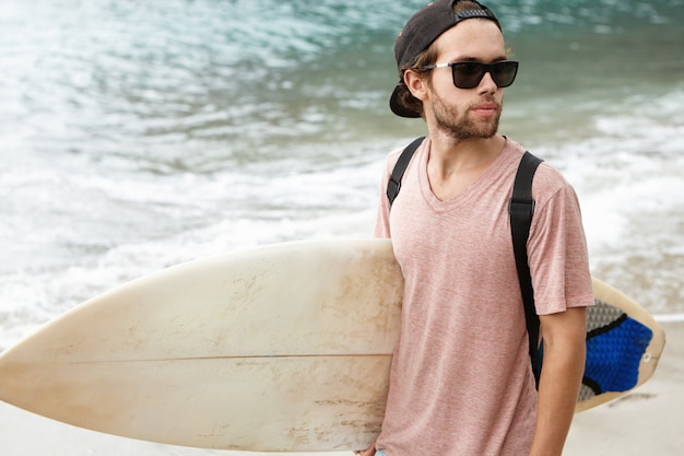 Summer vacations, people, and watersports concept. Fashionable young bearded man wearing shades and snapback