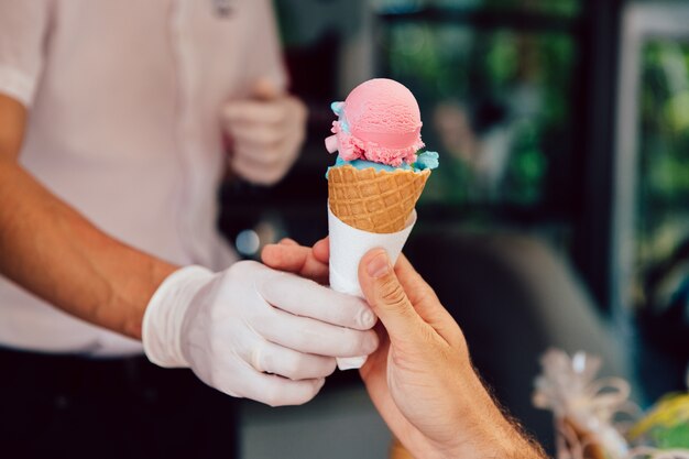 Summertime. Close-up view of man buying cone of ice-cream in kiosk, outdoors.