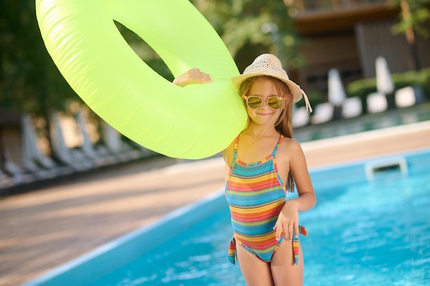 Summertime. Cute small girl with a yellow tube at the swimming pool