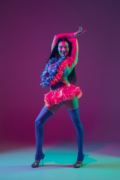 Summertime. Hawaiian brunette model on purple  wall in neon light. Beautiful women in traditional clothes smiling, dancing and having fun. Bright holiday's, celebration colors, festival.