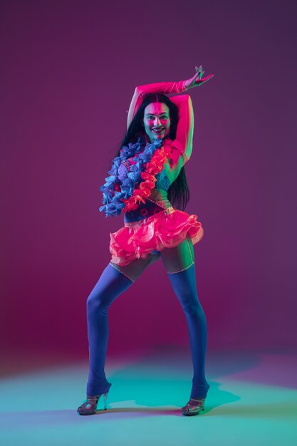 Summertime. Hawaiian brunette model on purple  wall in neon light. Beautiful women in traditional clothes smiling, dancing and having fun. Bright holiday's, celebration colors, festival.