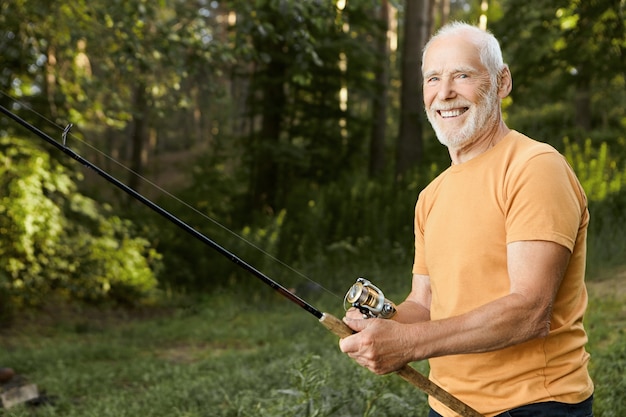 Summertime image of skilled fisherman on retirement having rest in wild nature using fishing rod, waiting for fish to be caught