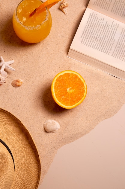 Free photo summertime vibes with book and hat on sand