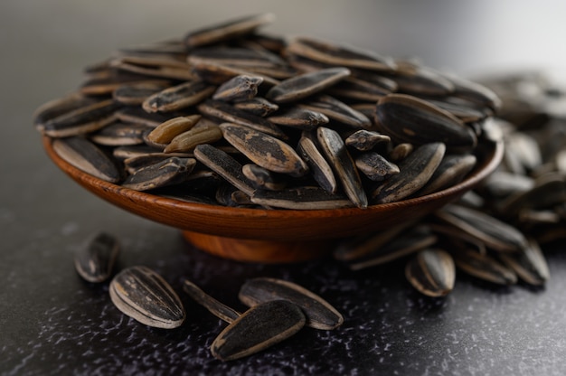 Free photo sun flower seed in a wooden bowl on the black cement floor.