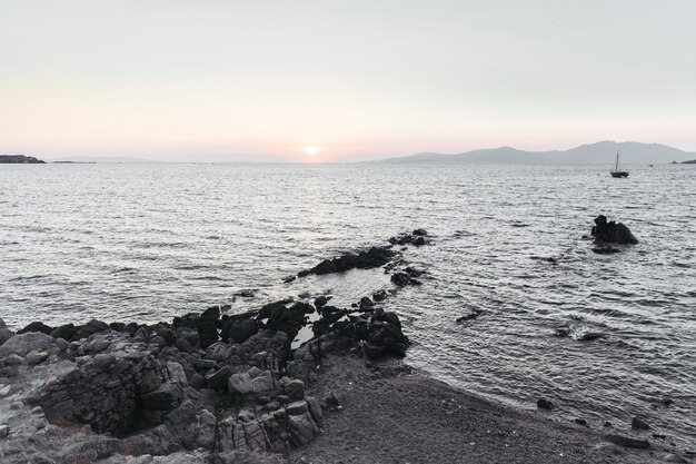 太陽は海に沈み、その前に黒い岩が