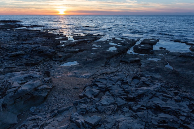 Sole che tramonta sulla riva con formazioni rocciose nel mare adriatico a savudrija, istria, croazia