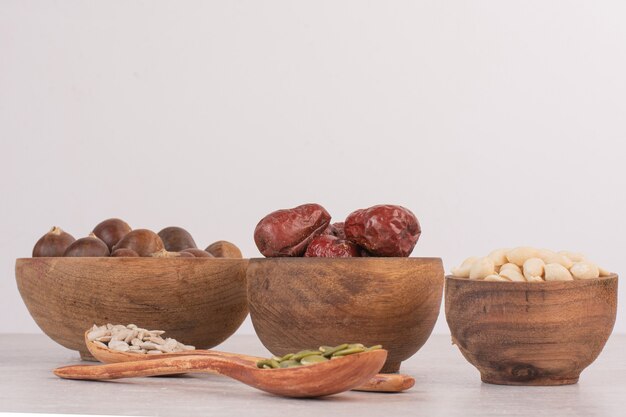 Sunflower and pumpkin seeds and bowls of nuts on white surface.