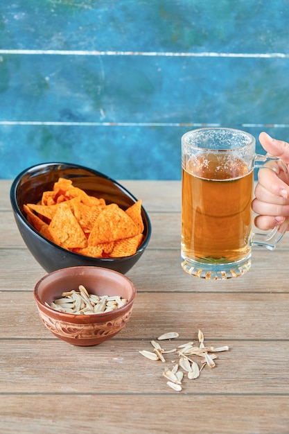 Sunflower seeds, a bowl of chips and a glass of beer on wooden table.