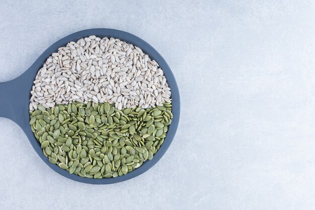 Sunflower seeds and pepitas assorted on a small serving pan on marble background.