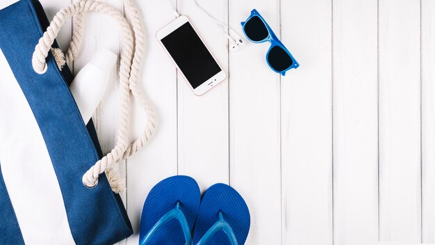 Sunglasses and smartphone near bag and flip-flops