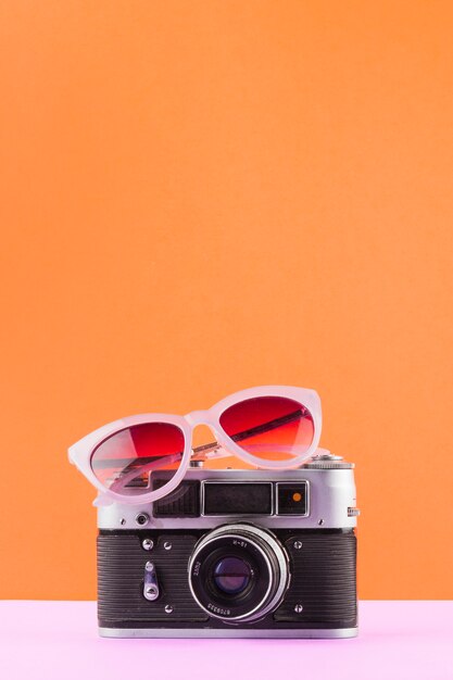 Солнцезащитные очки над винтажной камерой на белом столе на оранжевом фоне