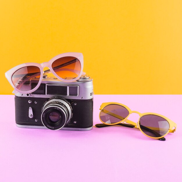 Sunglasses with camera on pink desk against yellow backdrop