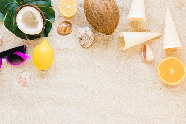 Sunglasses with exotic fruits and shells on sand