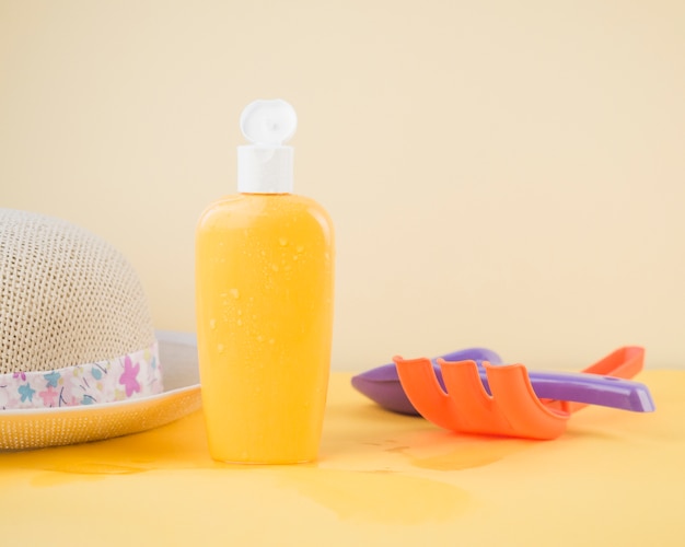 Sunhat; sunscreen bottle; rake and shovel toy against colored backdrop