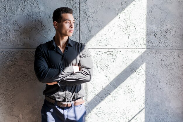 Sunlight falling over the serious young man standing against concrete wall