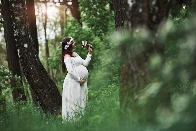 Sunlight and flowers. Beautiful pregnant woman in dress have a walk outdoors. Positive brunette