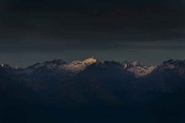 Foto gratuita luce solare che splende una cima della singola montagna al tramonto con il cielo nuvoloso scuro