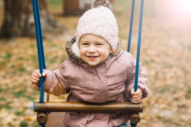 Sunlit little girl in warm clothes on swing 
